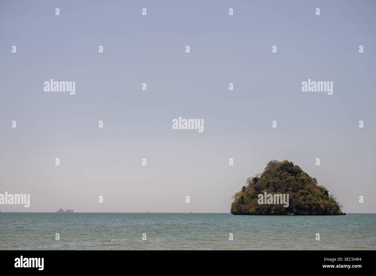 Piccola isola di pietra calcarea sorge dal tranquillo mare tropicale sotto il cielo limpido a Krabi in Thailandia Foto Stock
