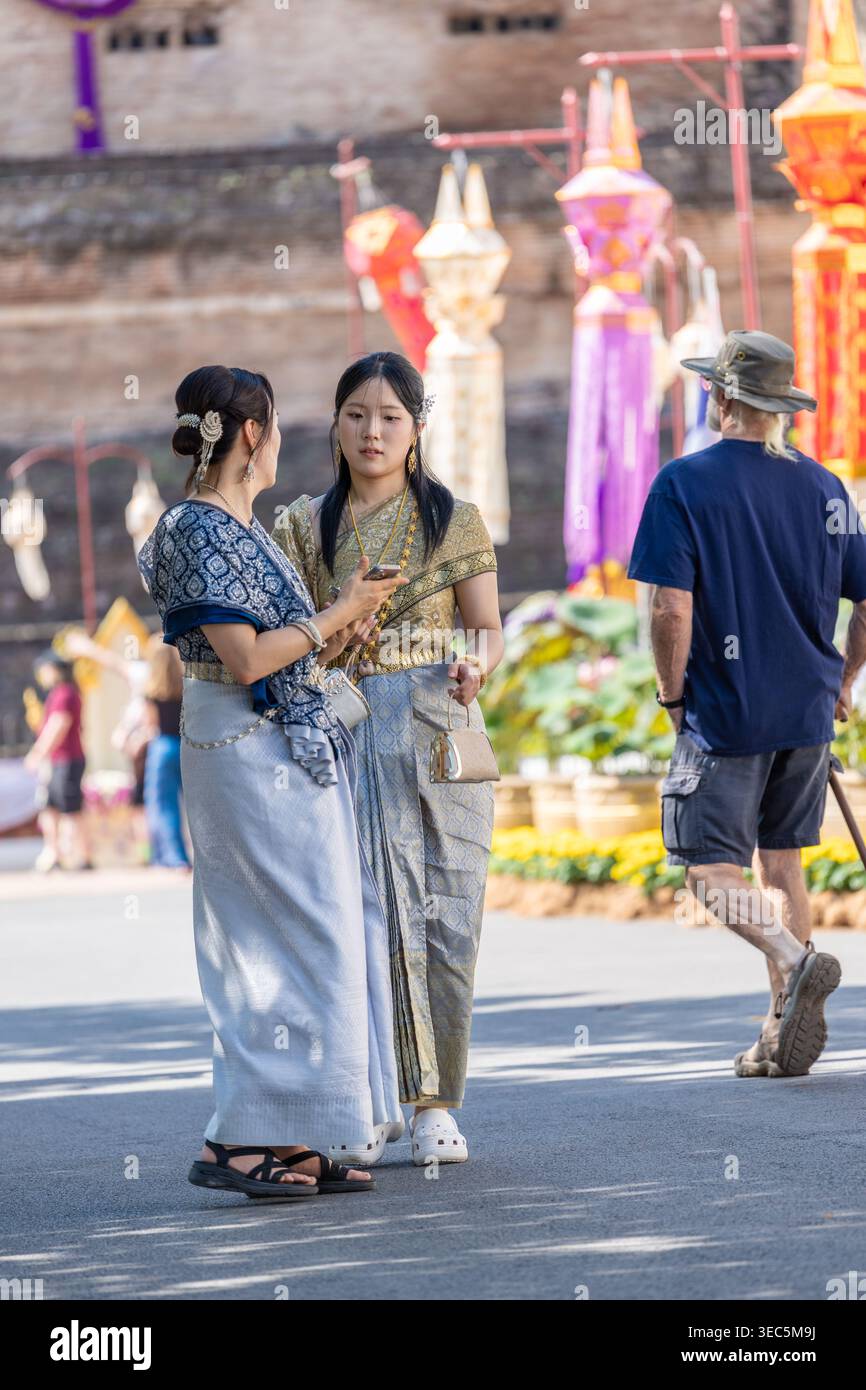 Bangkok, Thailandia - 22 gennaio 2026: Due donne in elegante abito tradizionale thailandese conversano tra lanterne colorate in un evento culturale o tempio, emb Foto Stock