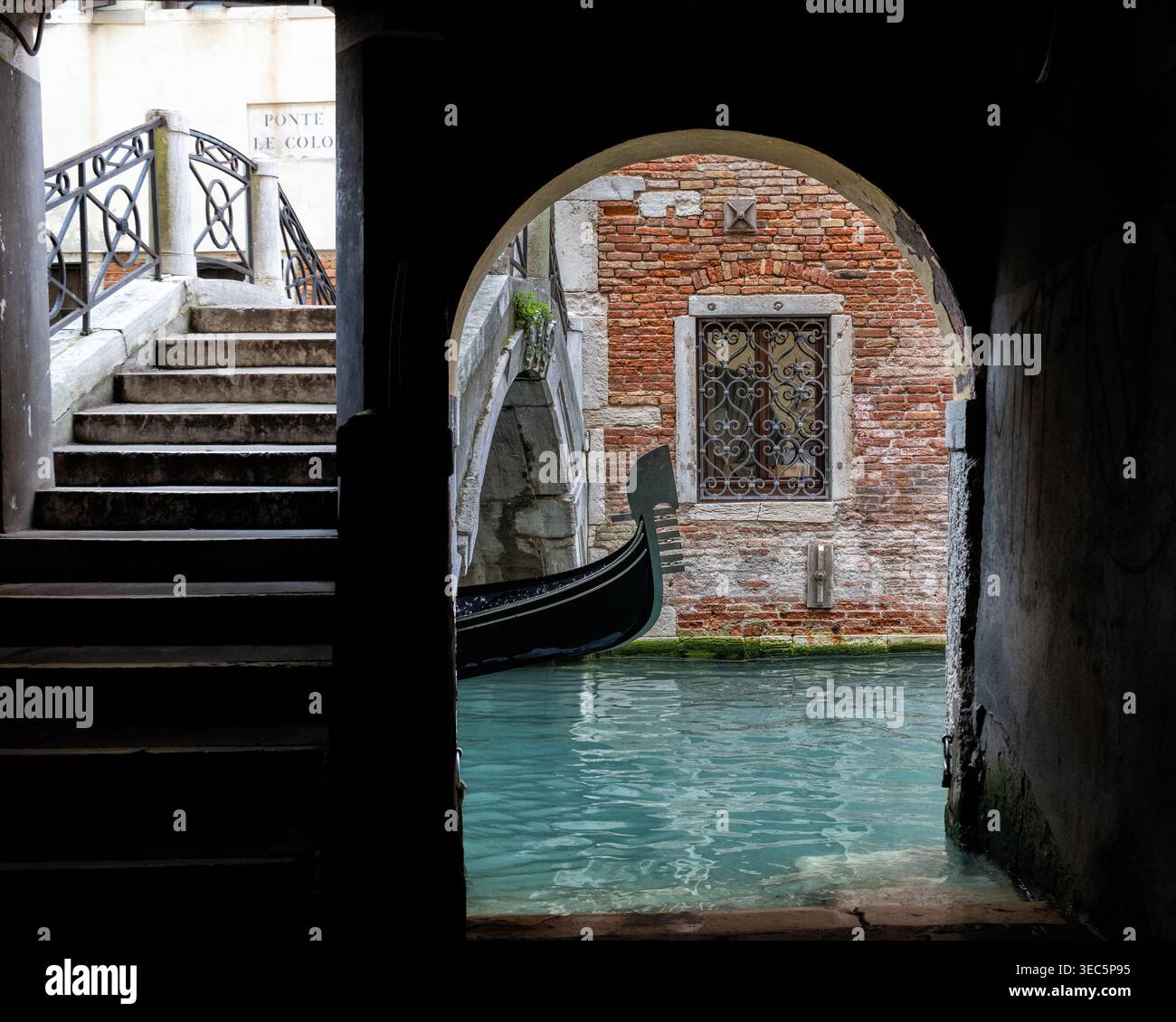 Venezia, Italia, gondola tradizionale che passa sotto un ponte storico su un canale veneziano stretto, una scena classica della famosa città lagunare. Foto Stock