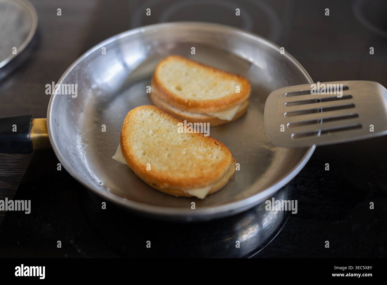 I panini grigliati si mescolano in una padella. Il pane dorato suggerisce una tostatura perfetta. La spatola in metallo poggia accanto alla teglia. Punti salienti della vista ravvicinata Foto Stock