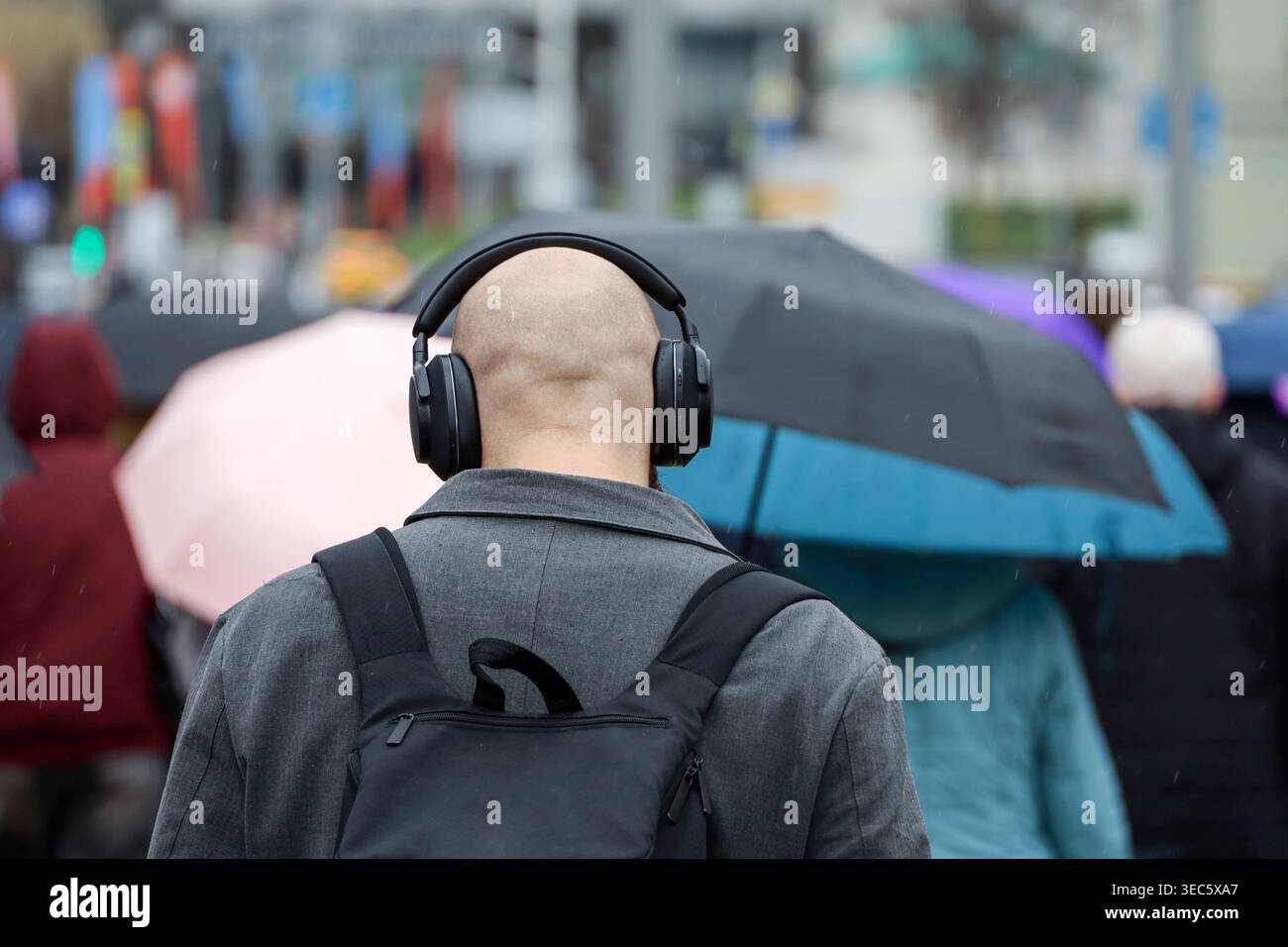 Uomo in cuffia che cammina sullo sfondo di persone con ombrelli, piove in città Foto Stock