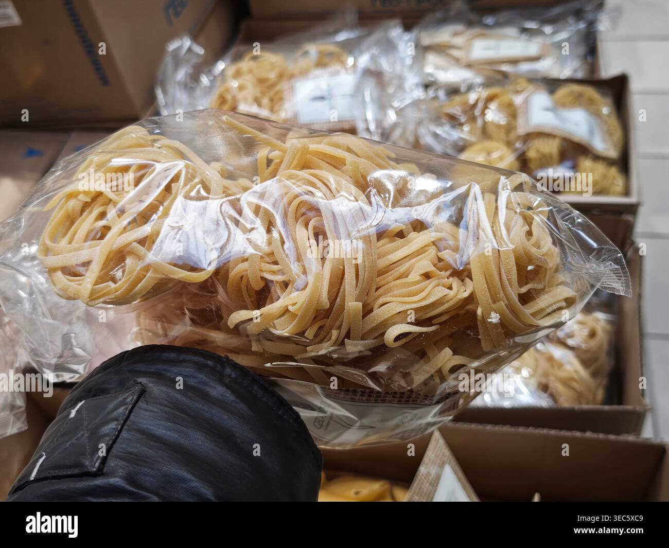 Un acquirente seleziona un sacchetto di pasta da un espositore in un negozio. Le scatole circostanti contengono diversi elementi. Foto Stock