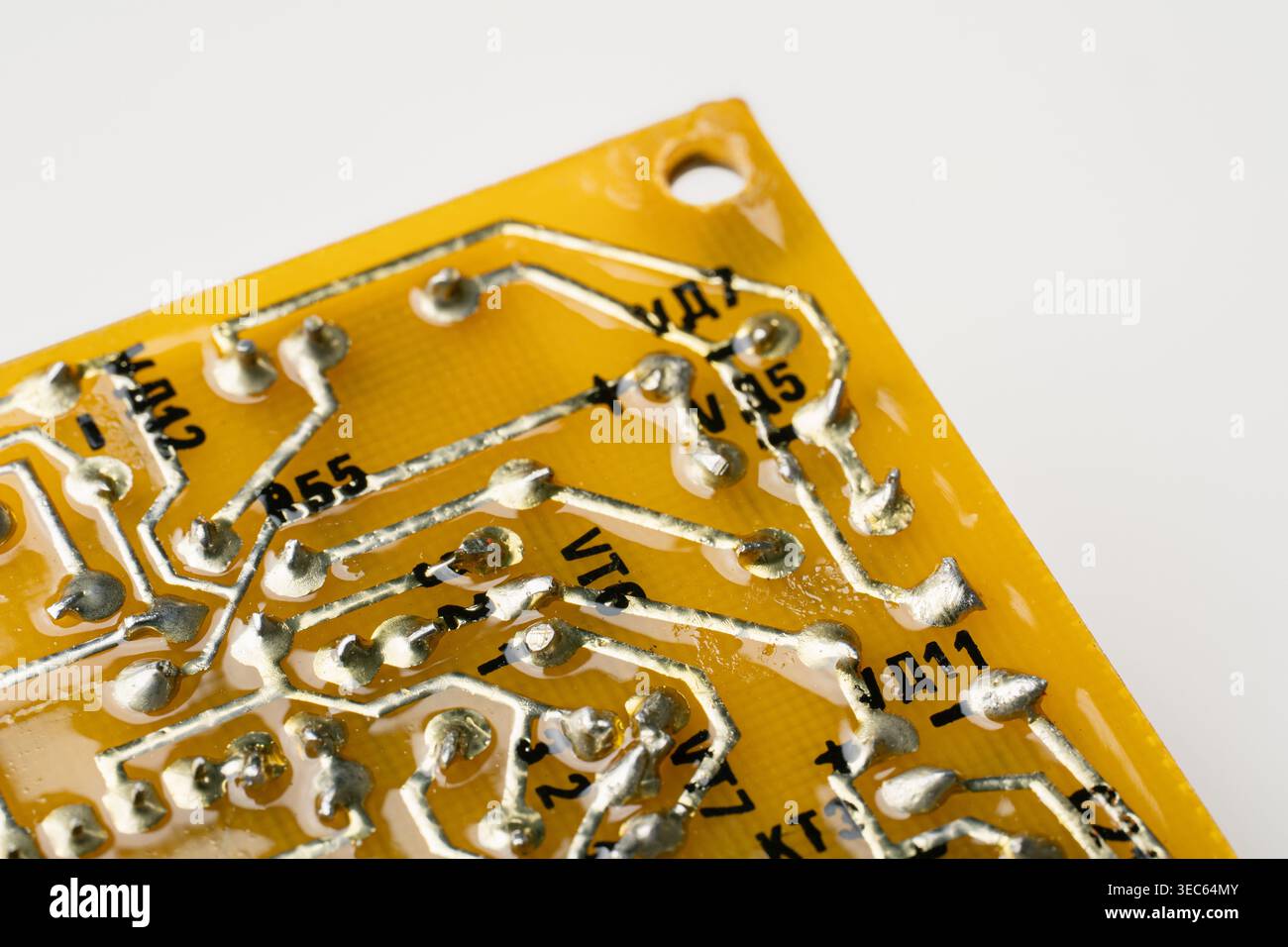 Macro-fotografia di giunti a saldare e tracce di rame su una scheda a circuito stampato gialla. Background tecnico di percorsi elettronici e saldature manuali Foto Stock