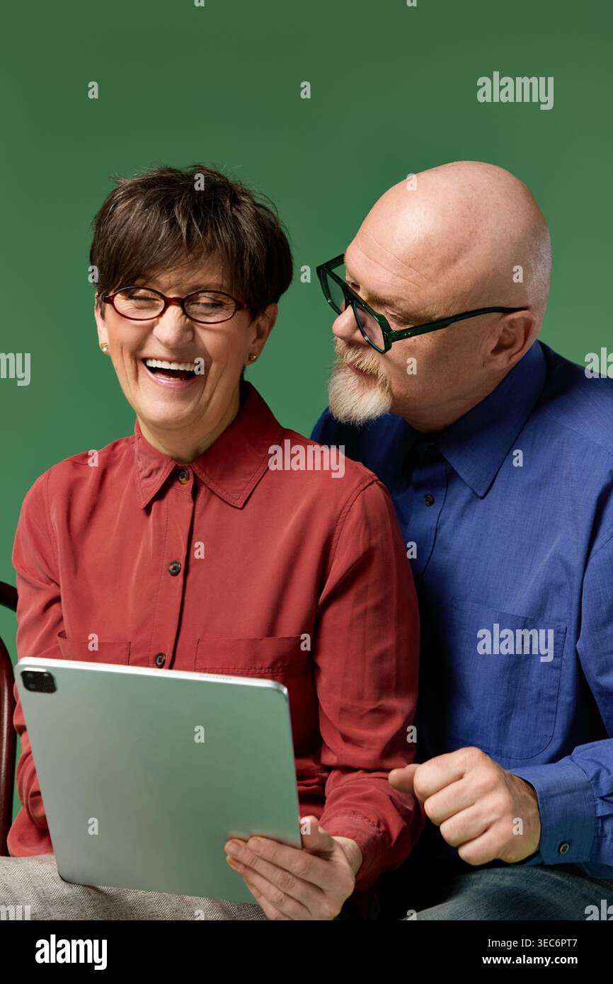 Una coppia di anziani allegra si diverte a ridere e a scoprire cose nuove su un tablet. Foto Stock