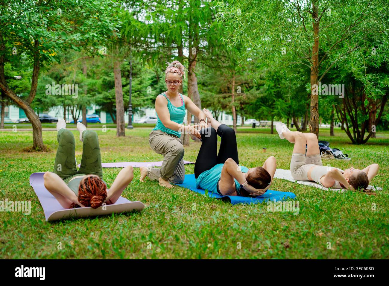 Donne che fanno i crunches sui tappetini con la guida di un istruttore nella classe di fitness Green Summer Park. Crunch, yoga, tappetini, istruttore, parco. Foto Stock