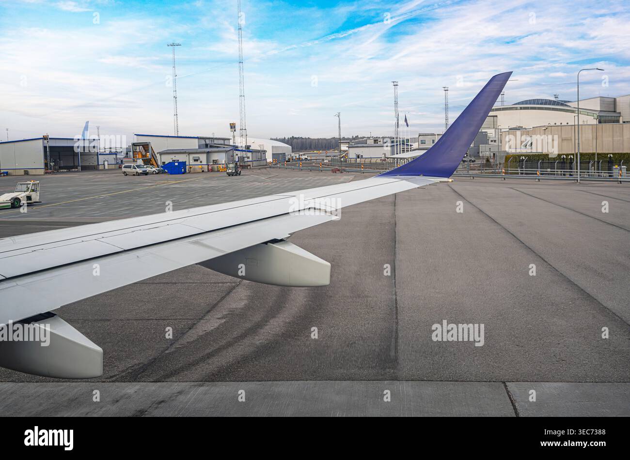 Una vista dalla finestra di un aereo mostra un'ala bianca con un'aletta blu parcheggiata su un asfalto dell'aeroporto. Foto Stock