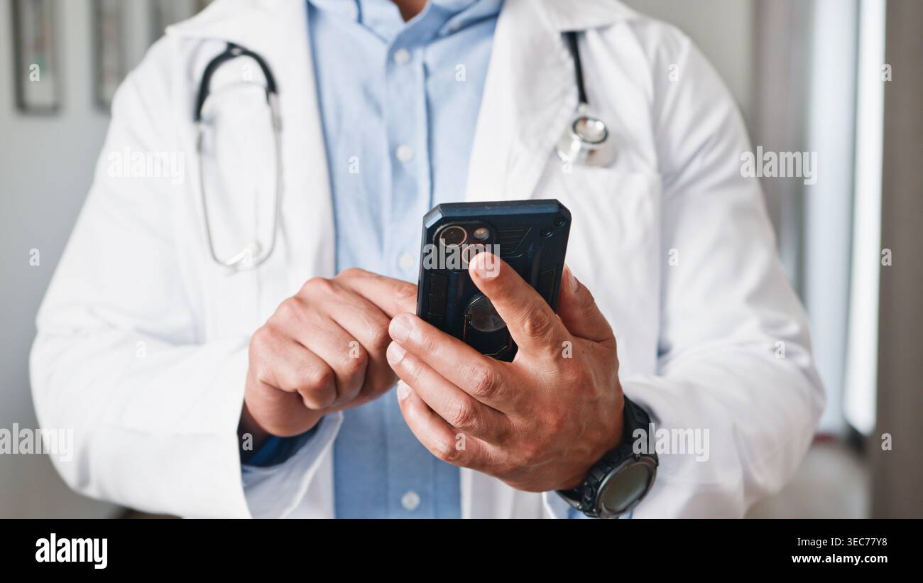 Medico che utilizza lo smartphone per la comunicazione di telemedicina e le registrazioni dei pazienti in un ambiente clinico moderno Foto Stock