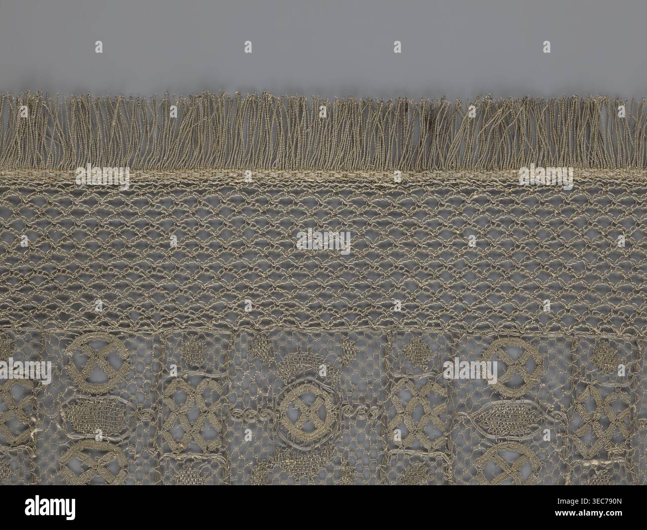 La cosiddetta cintura in pizzo sassone, la cintura in pizzo come accessorio di abbigliamento maschile. La parte centrale è una cintura continua con un ornamento geometrico; tra i motivi c'è un cerchio contenente una clessidra. Le cinghie laterali di larghezza simile sono collegate in modo permanente. L'intero nastro è rifilato con frange. XVII/XVIII secolo, Polonia. Materiali: pizzo; dimensioni: Altezza 270 cm, larghezza 25 cm., primo piano di un tessuto testurizzato che mostra una fascia orizzontale di frangia nella parte superiore e un intreccio aperto a rete sotto di essa, seguito da una sezione di pizzo a motivi geometrici ripetuti. I colori visibili sono beige e grigio, con Foto Stock