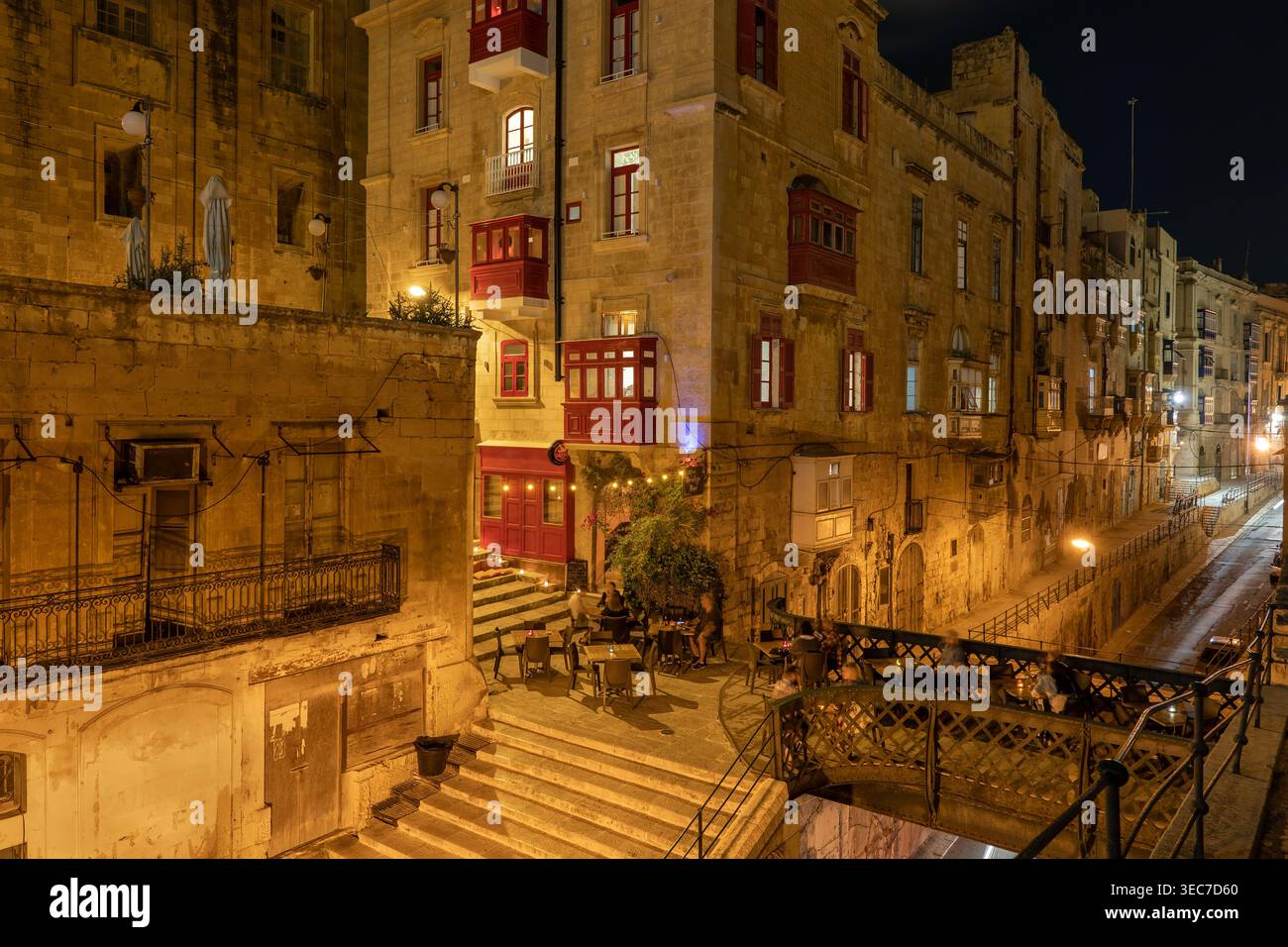 Città vecchia di la Valletta (il-Belt) di notte a Malta. Edifici tradizionali, ponte pedonale su via Liesse e persone ai tavoli all'aperto della Brid Foto Stock