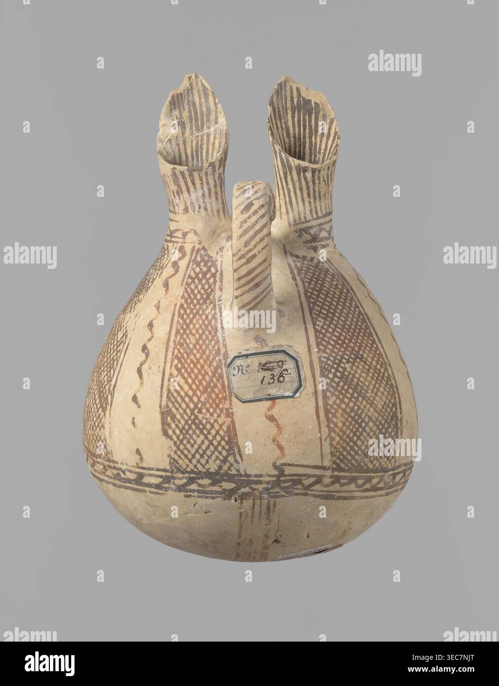 Caraffa, laboratorio cipriota sconosciuto. Caraffa bianca verniciata con fondo sferico, corpo sporgente a forma di pera che si trasforma nella parte superiore in due beccucci tubolari con pareti sporgenti. Tra di loro, una morsa ad anello sporge dal corpo. La nave è ricoperta di vernice bianca e decorata con vernice marrone-rossa. Un ornamento a zigzag corre intorno al corpo per 1/3 dell'altezza della nave, fiancheggiato su ciascun lato da due linee orizzontali. Di seguito sono riportate quattro bande di linee che convergono in basso. La parte superiore del corpo è decorata con quattro strisce piene di linee diagonali e intersecanti. Il Foto Stock