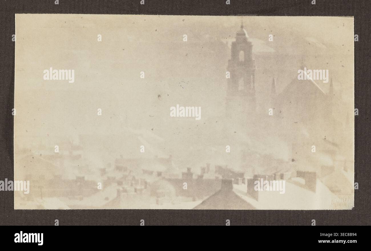 Chiesa di Ognissanti; Fotografia, 1912, panorama di Vilnius; fotografo Jan Bułhak 1876–1950. Stampa fotografica: 9,5 x 16,5 cm; pagina album: 31,0 x 23,5 cm., Una scena sbiadita dai toni seppia che mostra un paesaggio urbano nebulizzato con tetti in primo piano e un'alta struttura a torre con tetto a picco e guglie leggermente visibili sullo sfondo; il cielo e gli edifici si fondono in toni beige pallidi e marrone chiaro, con diverse macchie marroni più scure sparse sull'immagine e un bordo marrone scuro che incorniciano l'immagine. Foto Stock