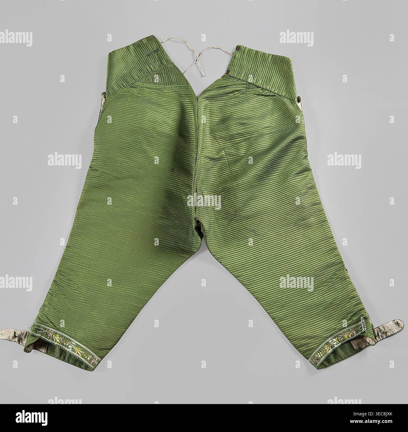 Pantaloni, motivi vegetali, motivi floreali, abbigliamento, moda, abbigliamento maschile, abbigliamento del xviii secolo. Pantaloni corti al ginocchio con patta, realizzati in tessuto di seta verde. Due piccole tasche sotto la patta. Grandi tasche ai lati. Due piccole tasche per portachiavi sopra la patta. Le gambe sono strette, fissate ai lati con sei bottoni ricamati. Schienale regolabile, legato con un nastro. Anni '1770, Slesia; Made in France, lunghezza 81 cm., Un paio di pantaloni verdi disposti su uno sfondo grigio chiaro, con una trama a coste o pieghe che corre orizzontalmente sul tessuto; l'area della cintura è Foto Stock