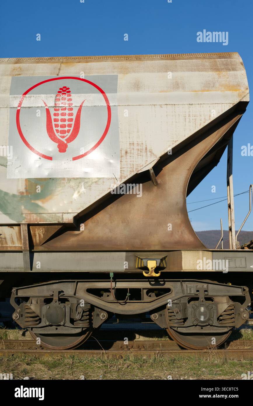 Profilo laterale di un vagone ferroviario con tramogge intemperie sui binari, con logo rosso di pannocchia all'interno di un cerchio, adagiato su un cielo blu limpido in una terra rurale Foto Stock