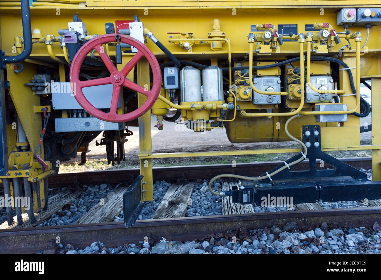Complesso assemblaggio di macchinari industriali con telai in acciaio giallo, una ruota di controllo manuale rossa e intricate tubazioni idrauliche sui binari ferroviari Foto Stock