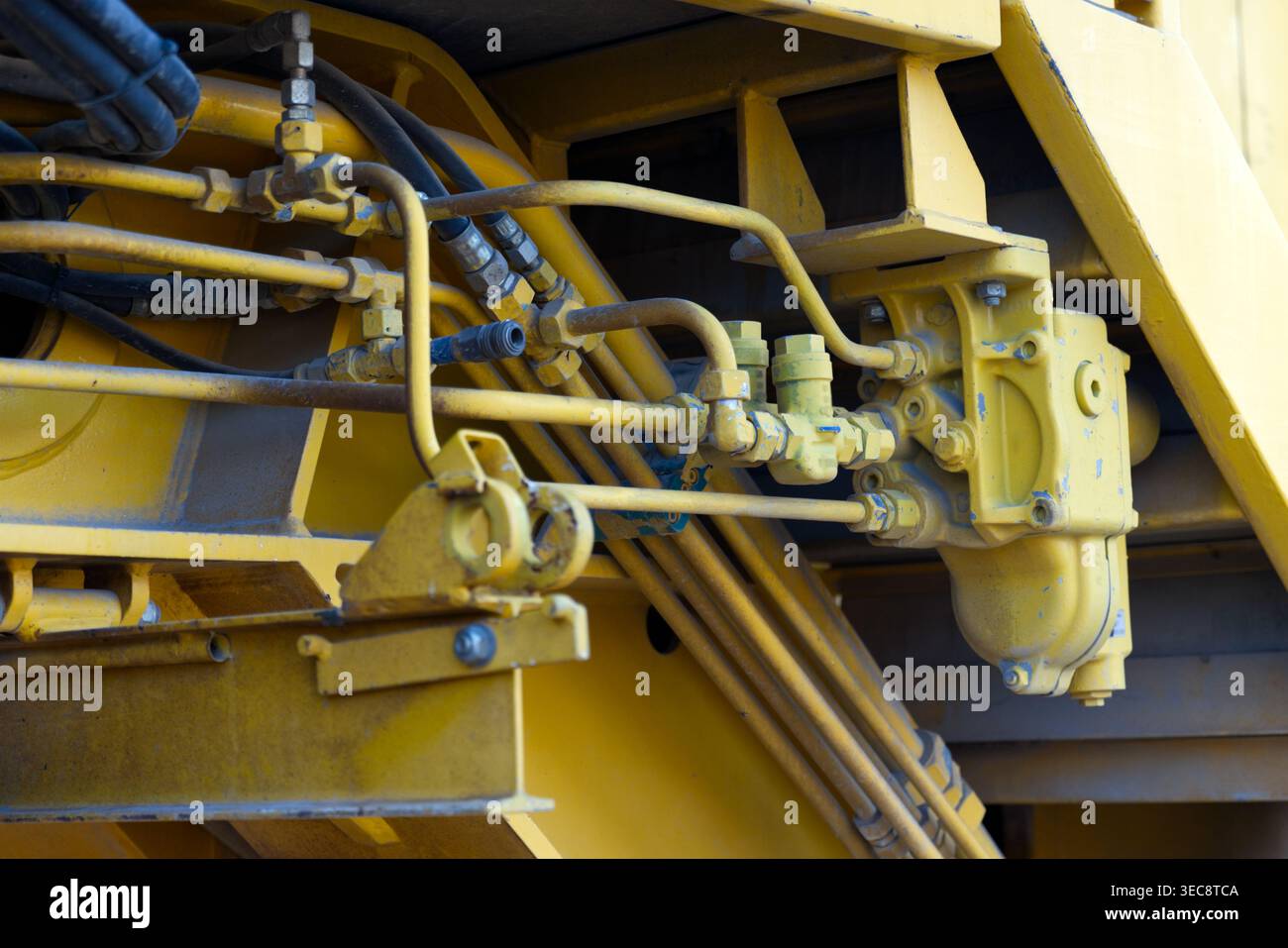 Una rete complessa di tubazioni idrauliche industriali e raccordi in metallo giallo su macchinari pesanti. Foto Stock