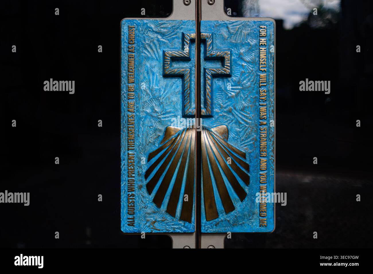 Primo piano dettagliato di una targa blu e di bronzo con motivo a croce e capesante con un'accogliente iscrizione cristiana all'ingresso del CH Foto Stock