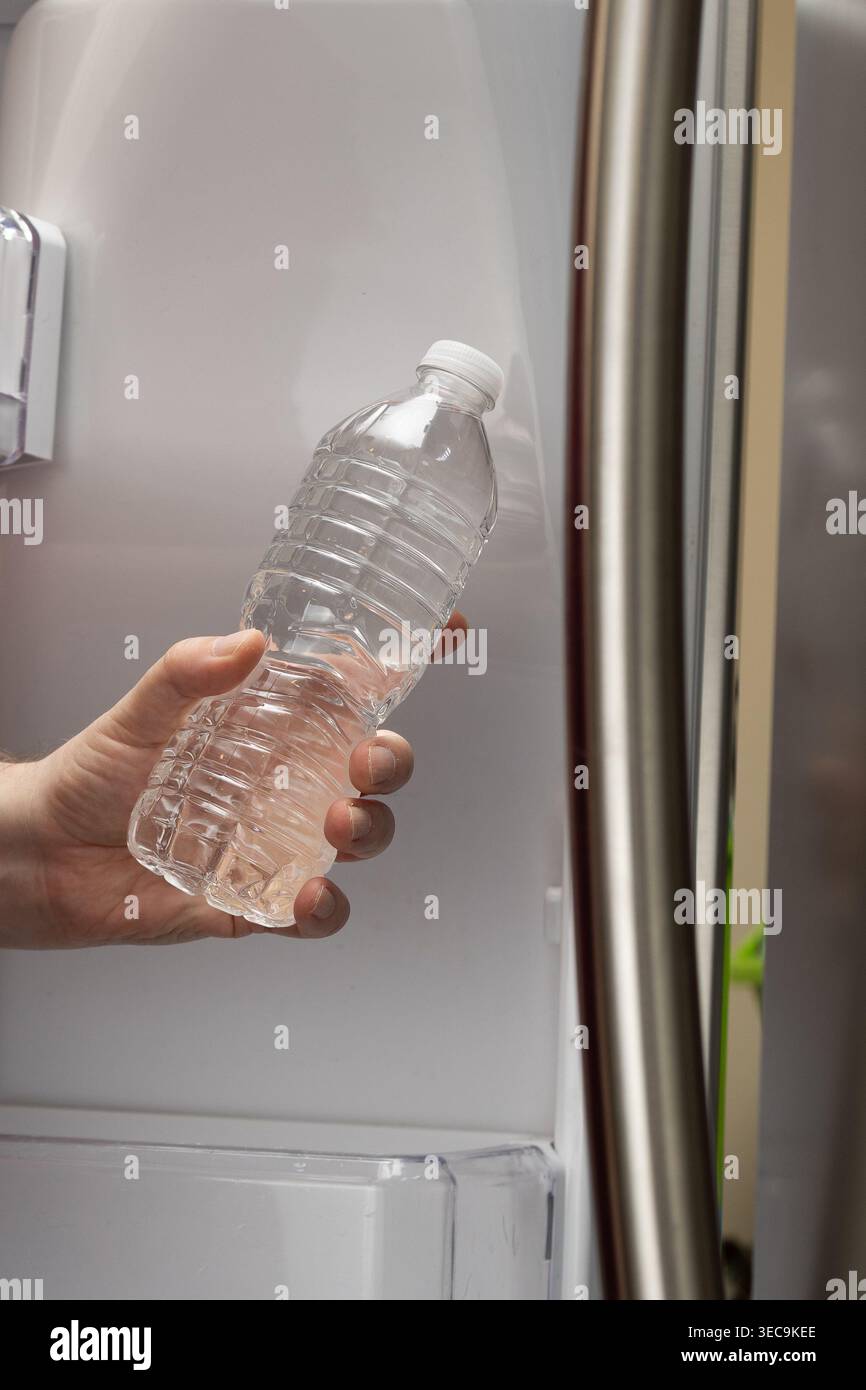 Primo piano verticale della mano per prelevare una bottiglia d'acqua dal frigorifero di casa Foto Stock