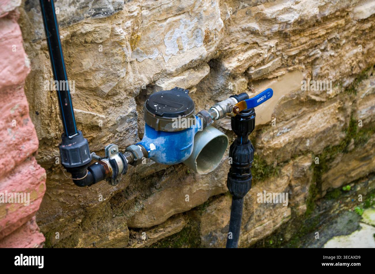 Misuratore dell'acqua per esterni con tubi e valvola su pareti in pietra Foto Stock