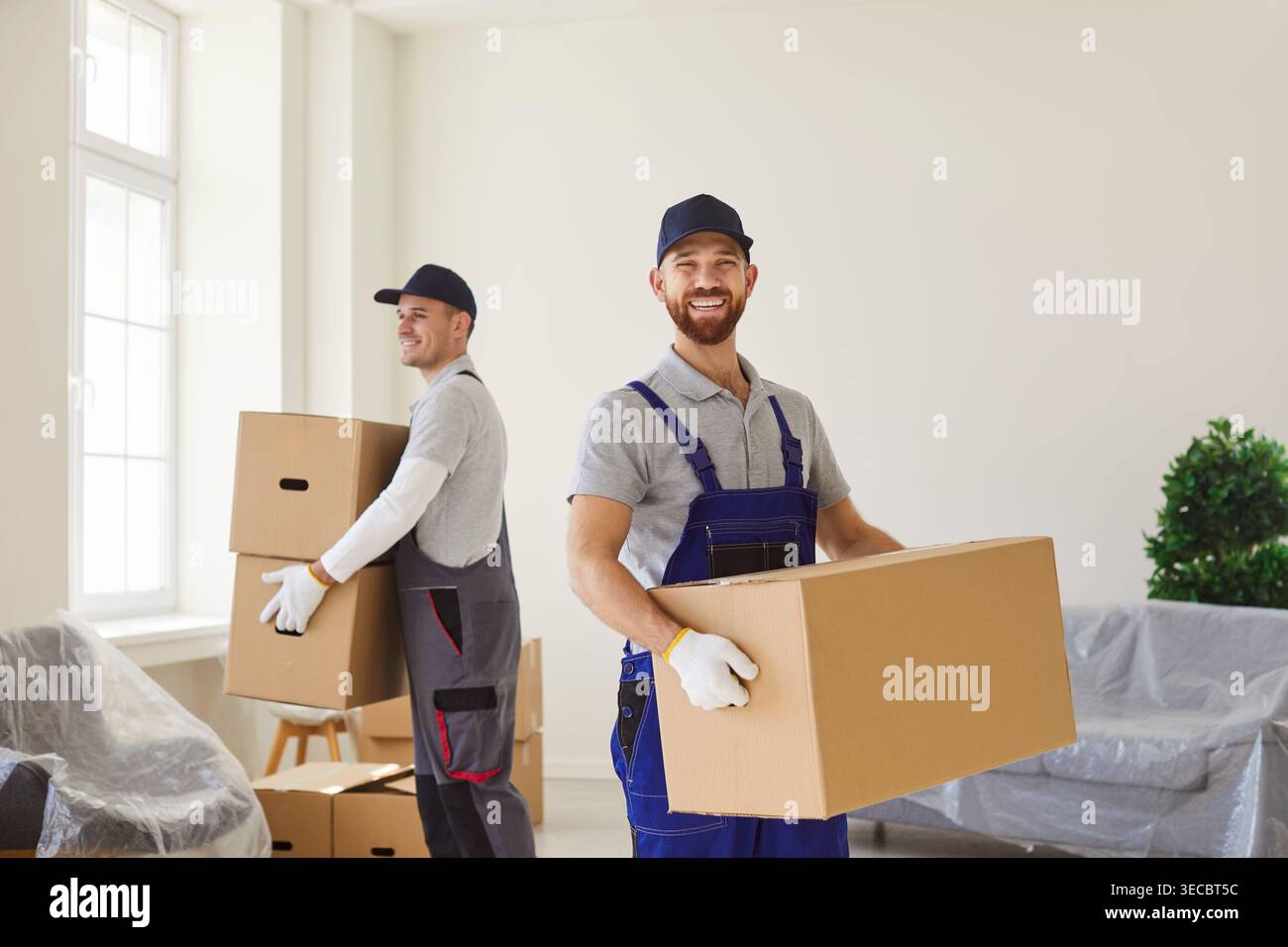 Due uomini del servizio di trasloco che trasportano scatole di cartone con effetti personali che aiutano i clienti a trasferirsi Foto Stock