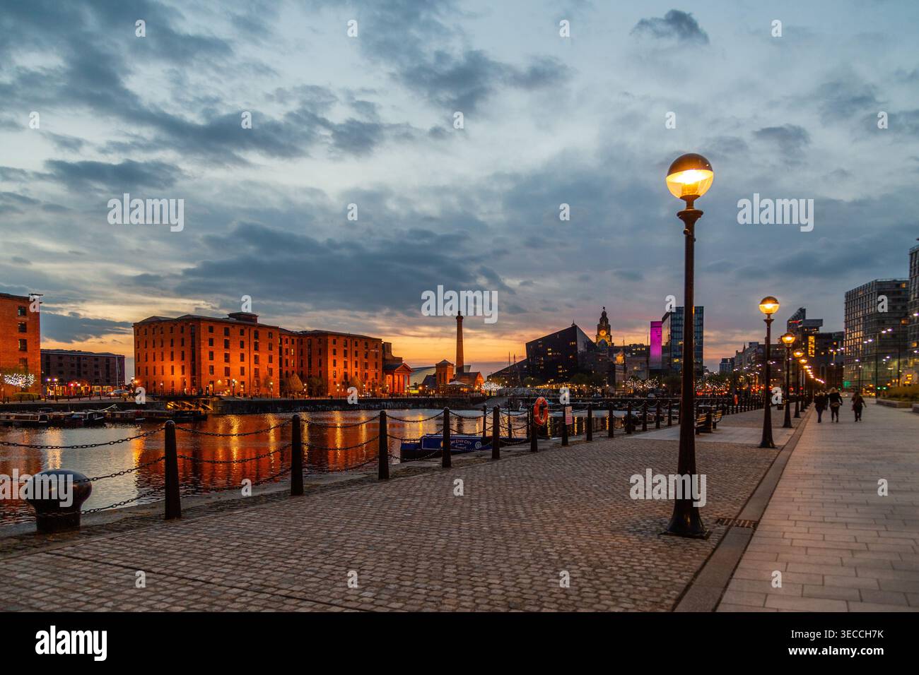 Royal Albert Dock Liverpool al tramonto, con gli storici magazzini di mattoni rossi, la passeggiata sul lungomare e lampioni luminosi al tramonto Foto Stock