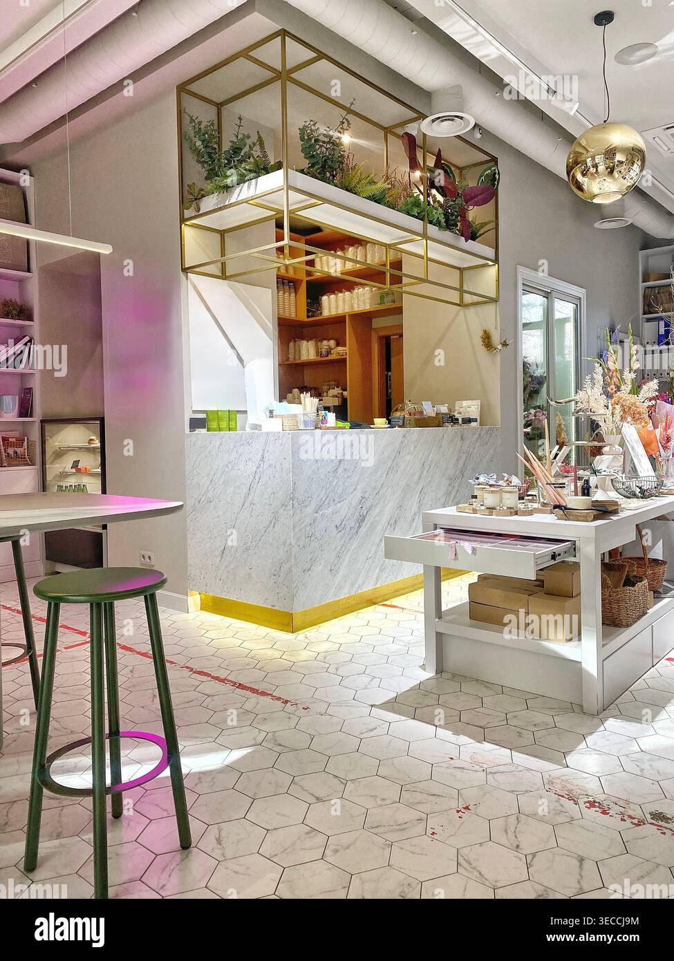 Interni moderni ed eleganti della caffetteria con banco in marmo, scaffali dorati, piante e illuminazione soffusa, design minimalista e contemporaneo della caffetteria - Immagine stock catturata con smartphone