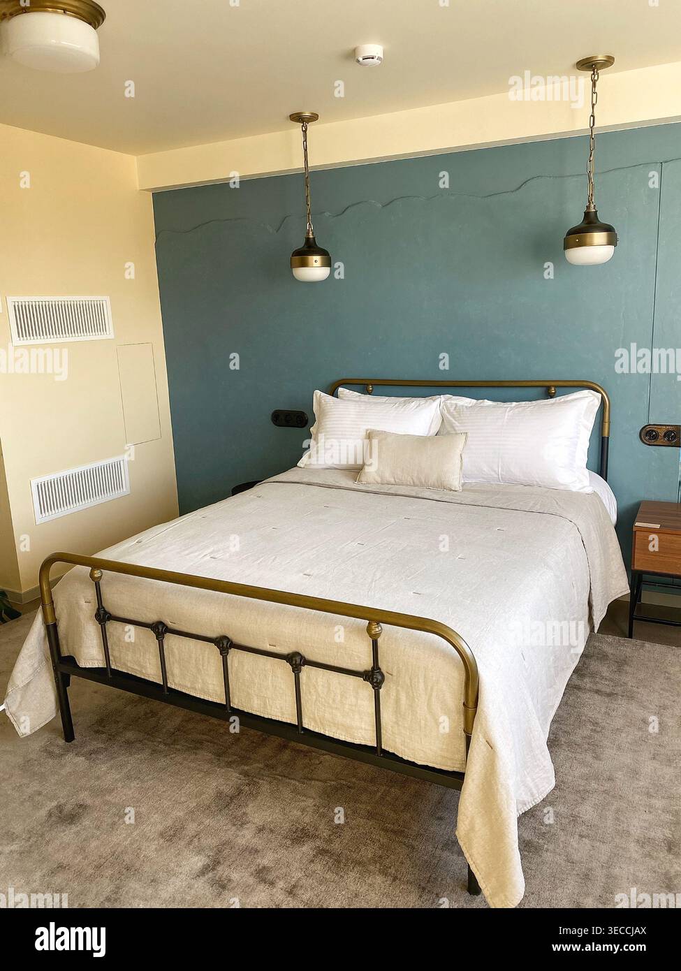 Interni moderni e accoglienti con letto doppio, soffici letti neutri e pareti con accenti blu, design minimalista e illuminazione calda - Immagine stock catturata con smartphone