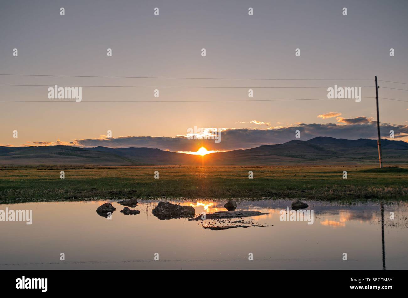 Tramonto su un lago tranquillo con montagne sullo sfondo e riflessi sull'acqua Foto Stock