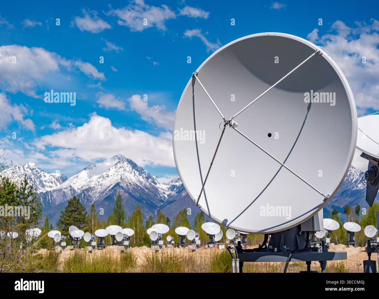 Il radiotelescopio si trova in un campo con montagne innevate sotto un cielo azzurro Foto Stock