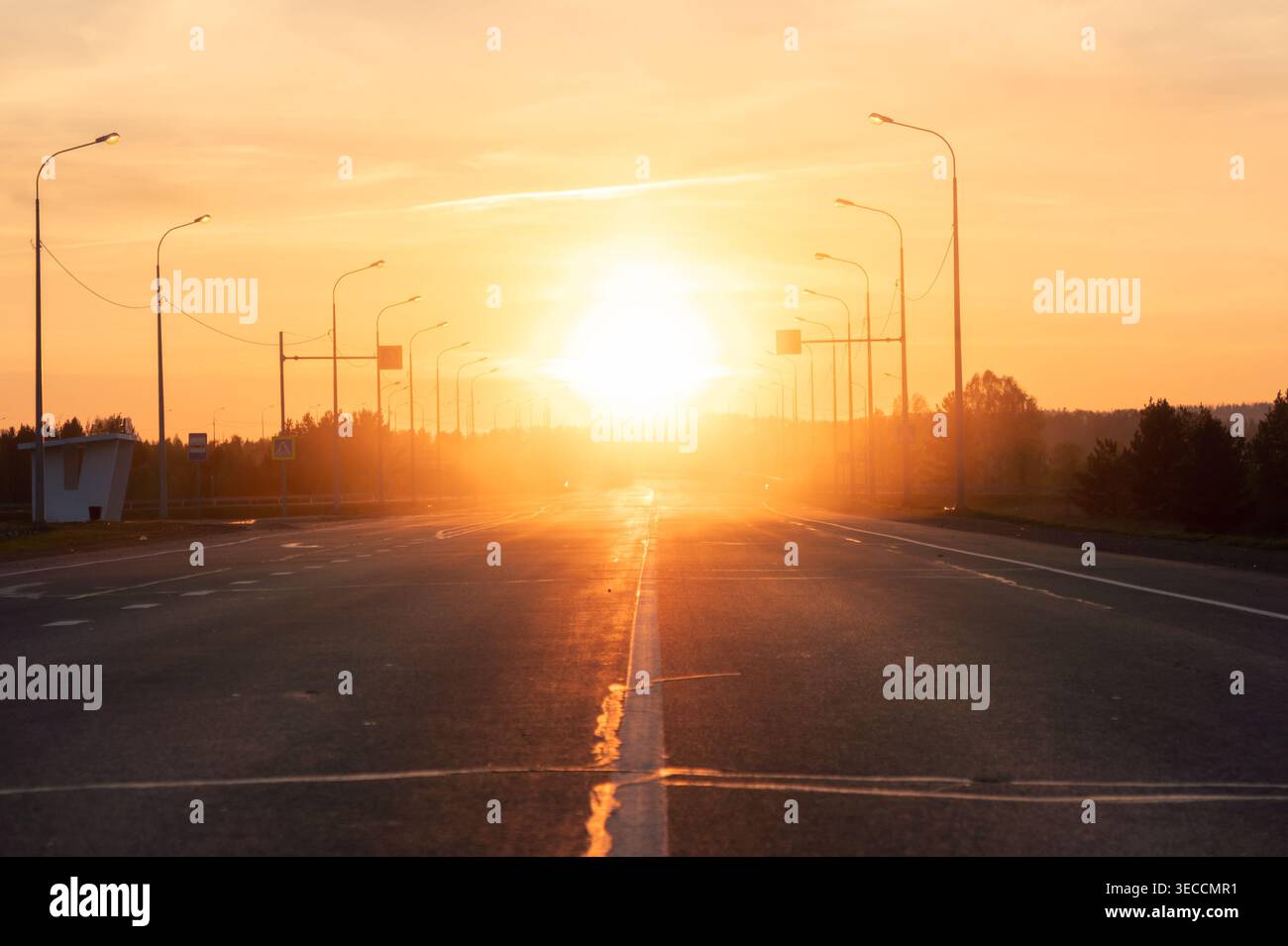La strada vuota si estende verso il sole che tramonta all'ora d'oro, fiancheggiata da una linea di semafori Foto Stock