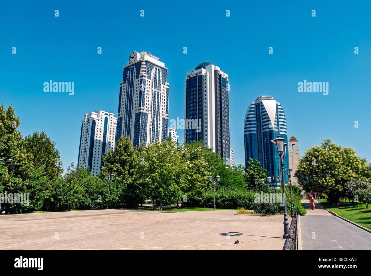 Grozny, Russia - 30 luglio 2021: Le moderne torri della città di Grozny si innalzano in un cielo blu luminoso sopra un parco urbano verdeggiante Foto Stock