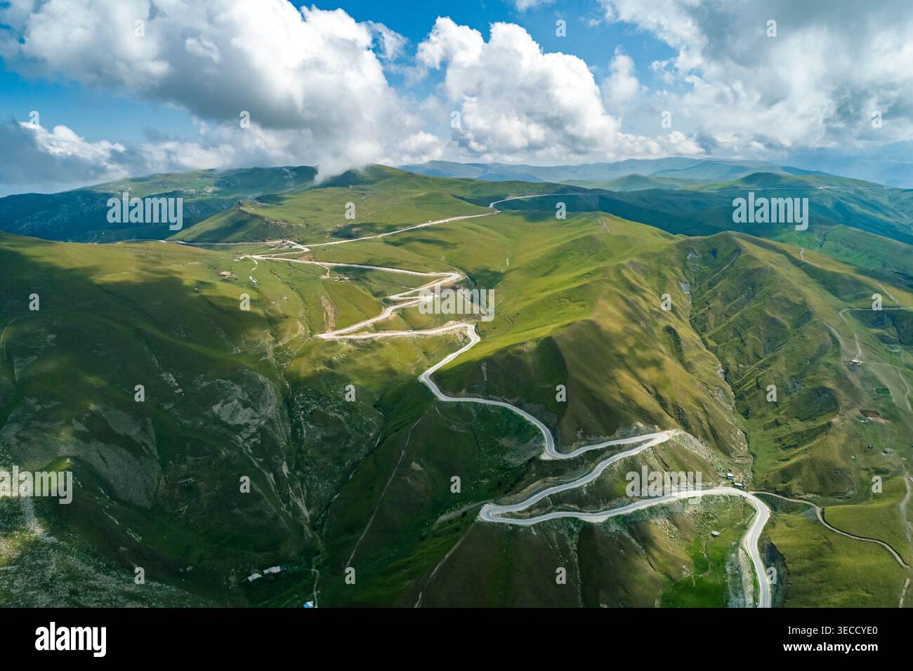 Vista panoramica della tortuosa strada di montagna che attraversa lussureggianti pendii verdi sotto un cielo luminoso Foto Stock
