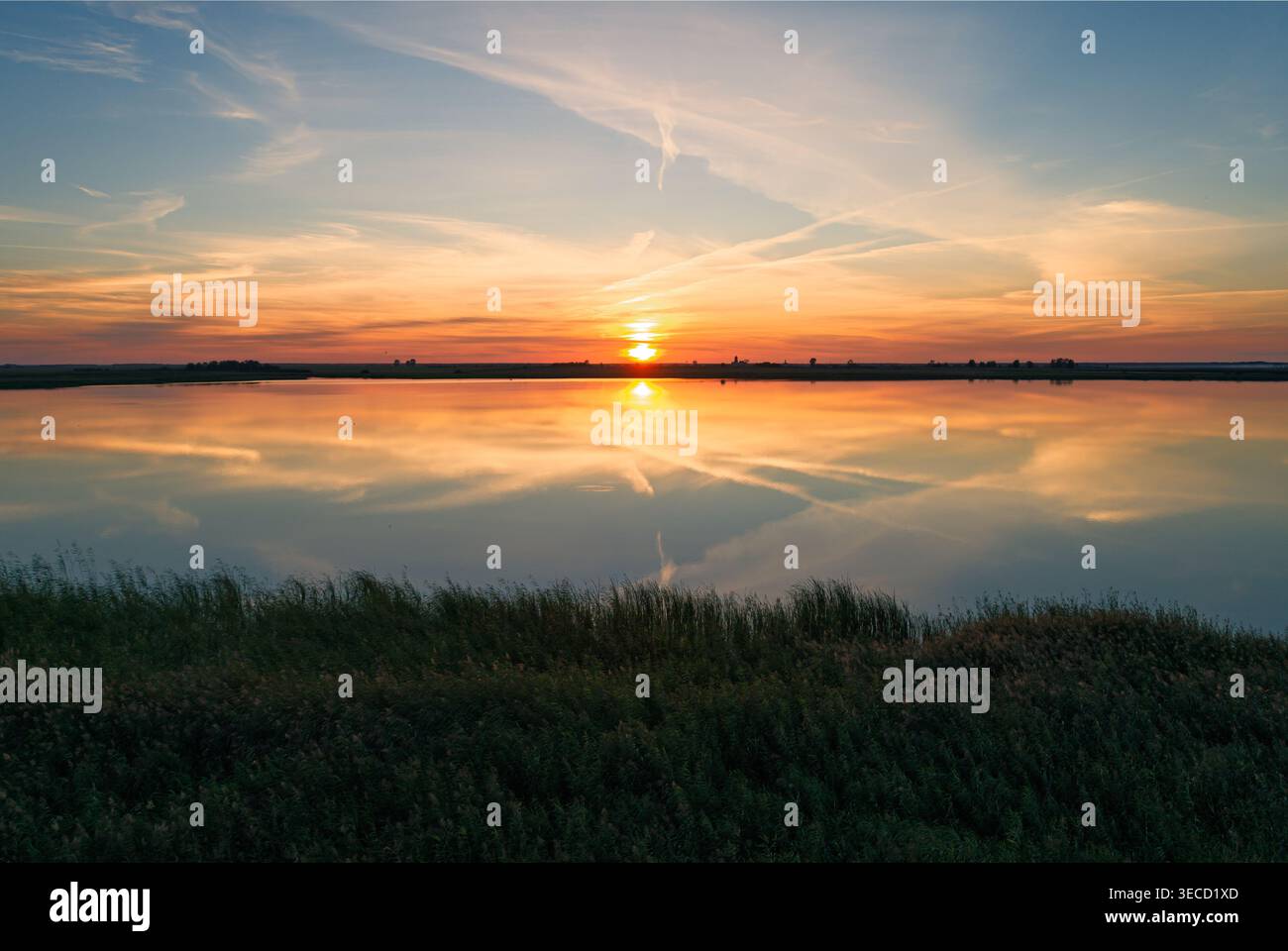 Il sole tramonta sullo splendido lago, proiettando un caldo bagliore sull'acqua e sul cielo Foto Stock