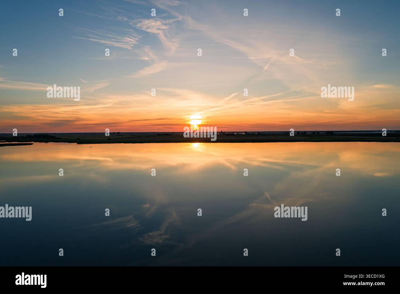 Il sole tramonta sullo splendido lago, proiettando un caldo bagliore sull'acqua e sul cielo Foto Stock