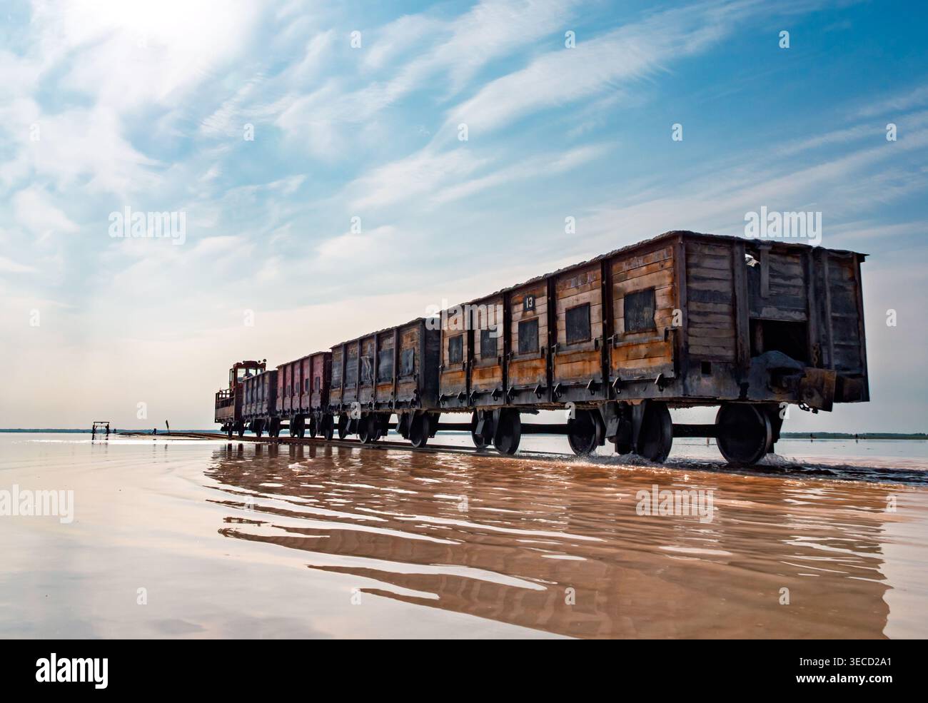 Locomotiva industriale Rusty che traina carri merci in legno attraverso acque rosa poco profonde a Bursol Lake Foto Stock