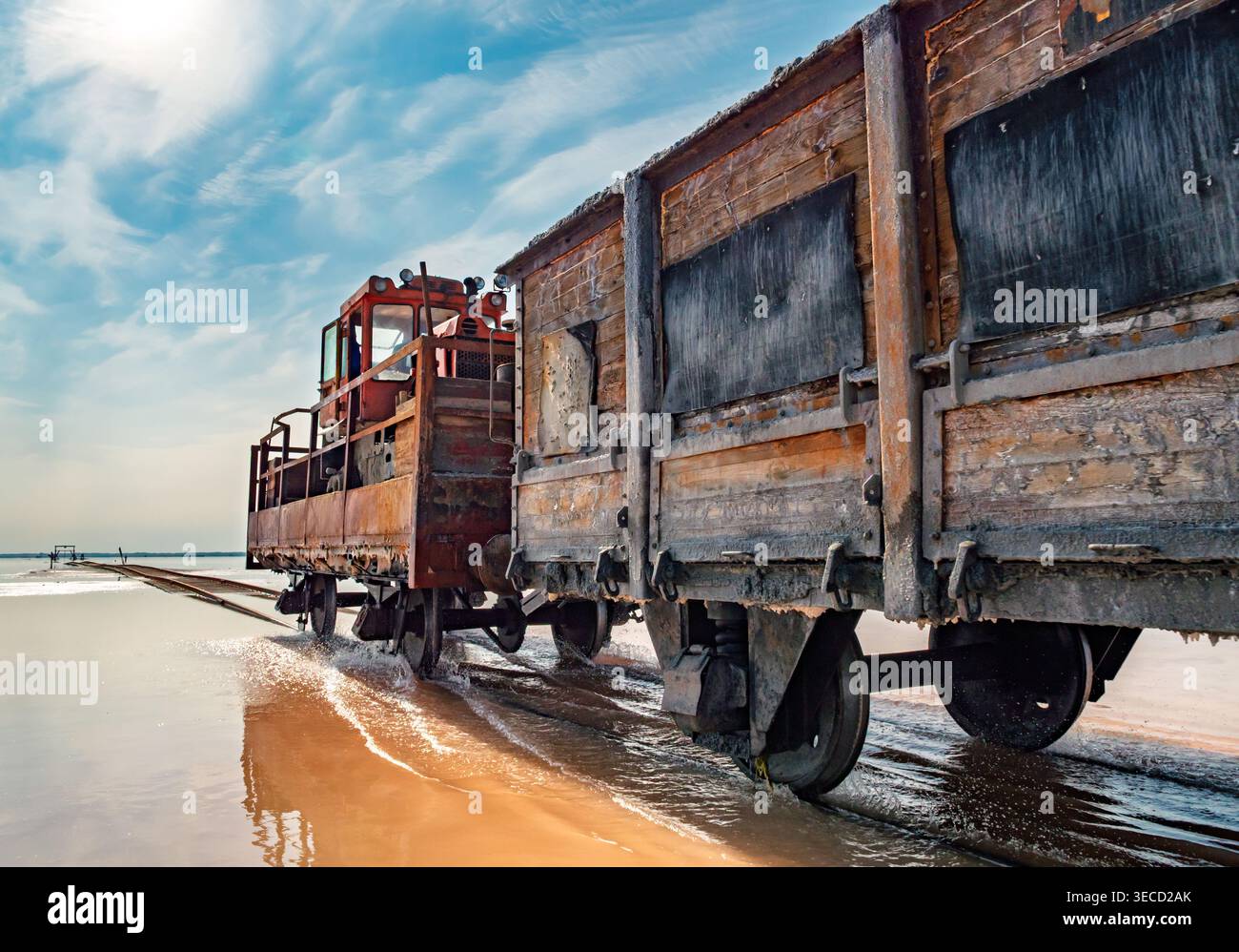 Locomotiva industriale Rusty che traina carri merci in legno attraverso acque rosa poco profonde a Bursol Lake Foto Stock