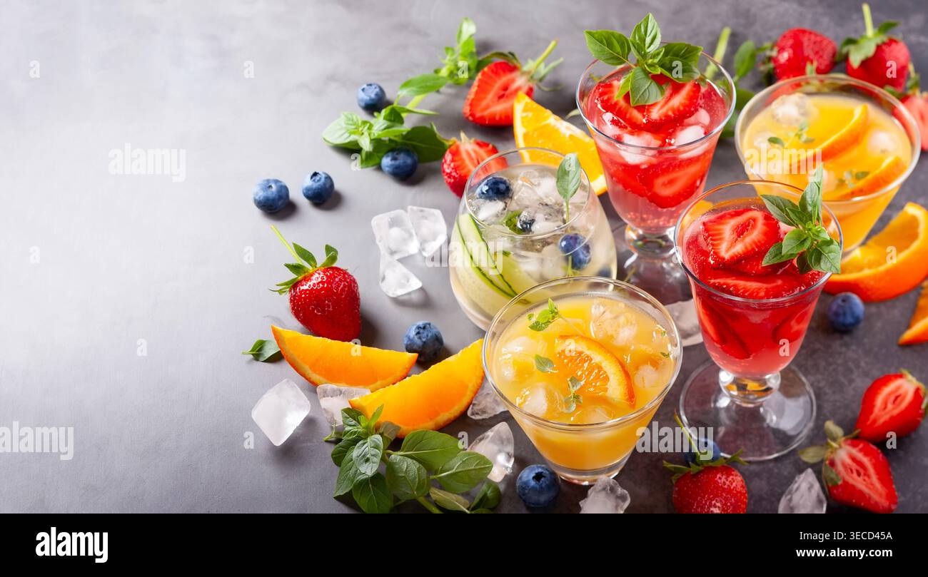Assortimento di cocktail analcolici estivi con bacche fresche, erbe e frutta su sfondo scuro. Foto Stock
