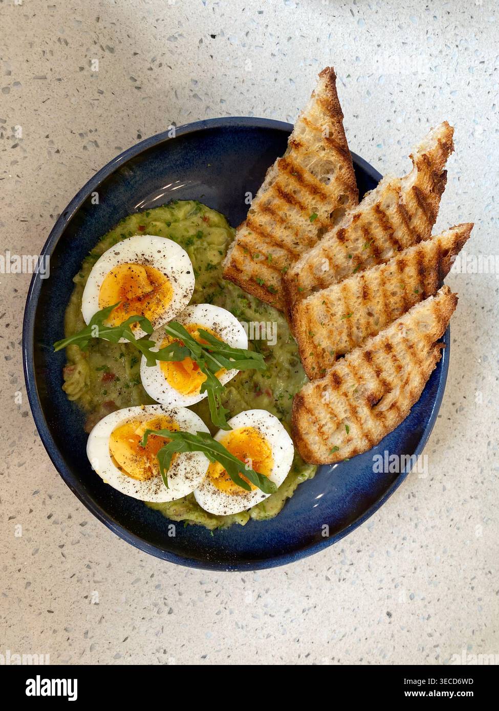 Avocado schiacciato con uova sode, accompagnato da toast alla griglia. Foto Stock