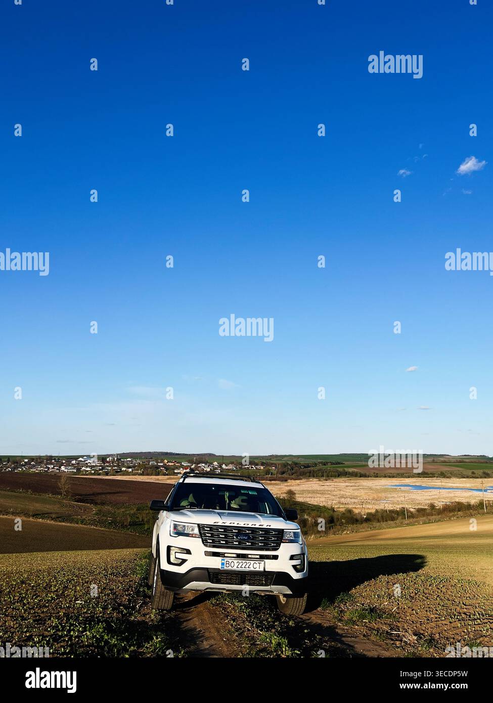 Kiev, Ucraina - 28 aprile 2026: SUV bianco Ford Explorer su una pista sterrata fuori strada nella campagna rurale sotto un cielo azzurro. Foto Stock