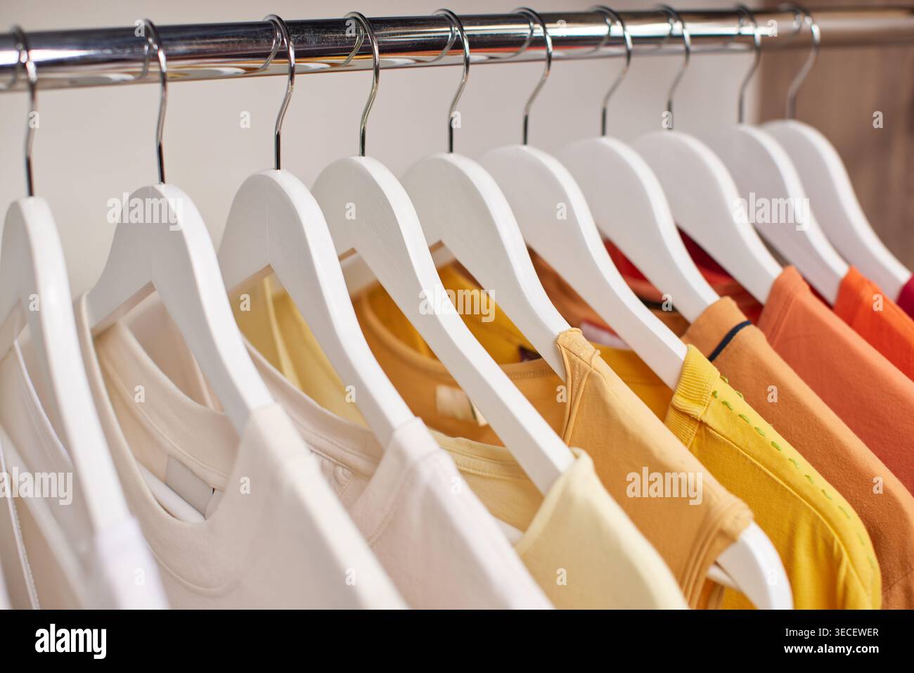 Fila di camicie di vari colori, dal bianco all'arancione, esposte su appendiabiti bianchi su un appendiabiti cromato Foto Stock