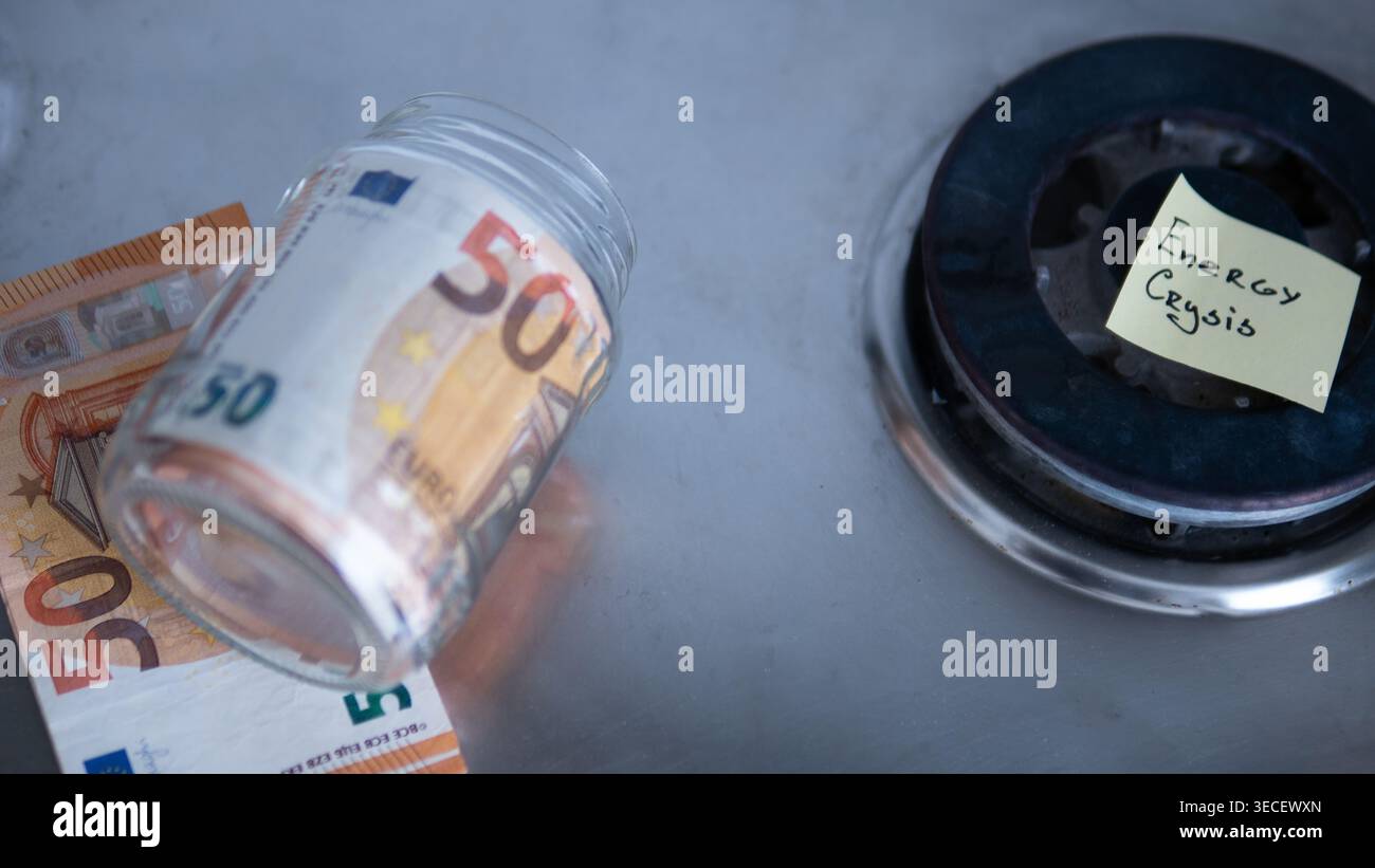 Vaso di moneta rovesciato con banconote in euro accanto a "crisi energetica" etichettato bruciatore a gas — concetto di rovina finanziaria Foto Stock