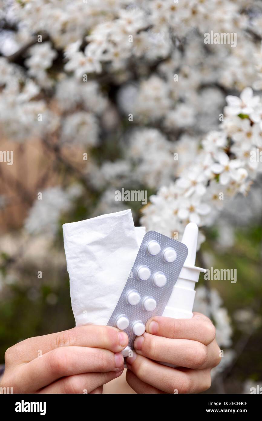 Bambino che tiene spray nasale, pillole e tessuti contro un albero in fiore. Allergia. Foto Stock