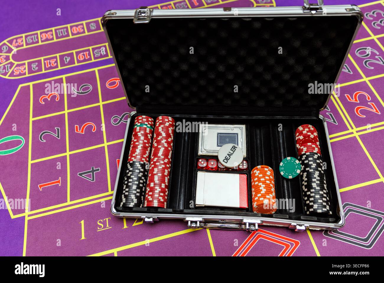 Una cassa aperta in alluminio piena di chip, dadi e carte da gioco poggiate su una superficie di casinò in feltro viola. Foto Stock