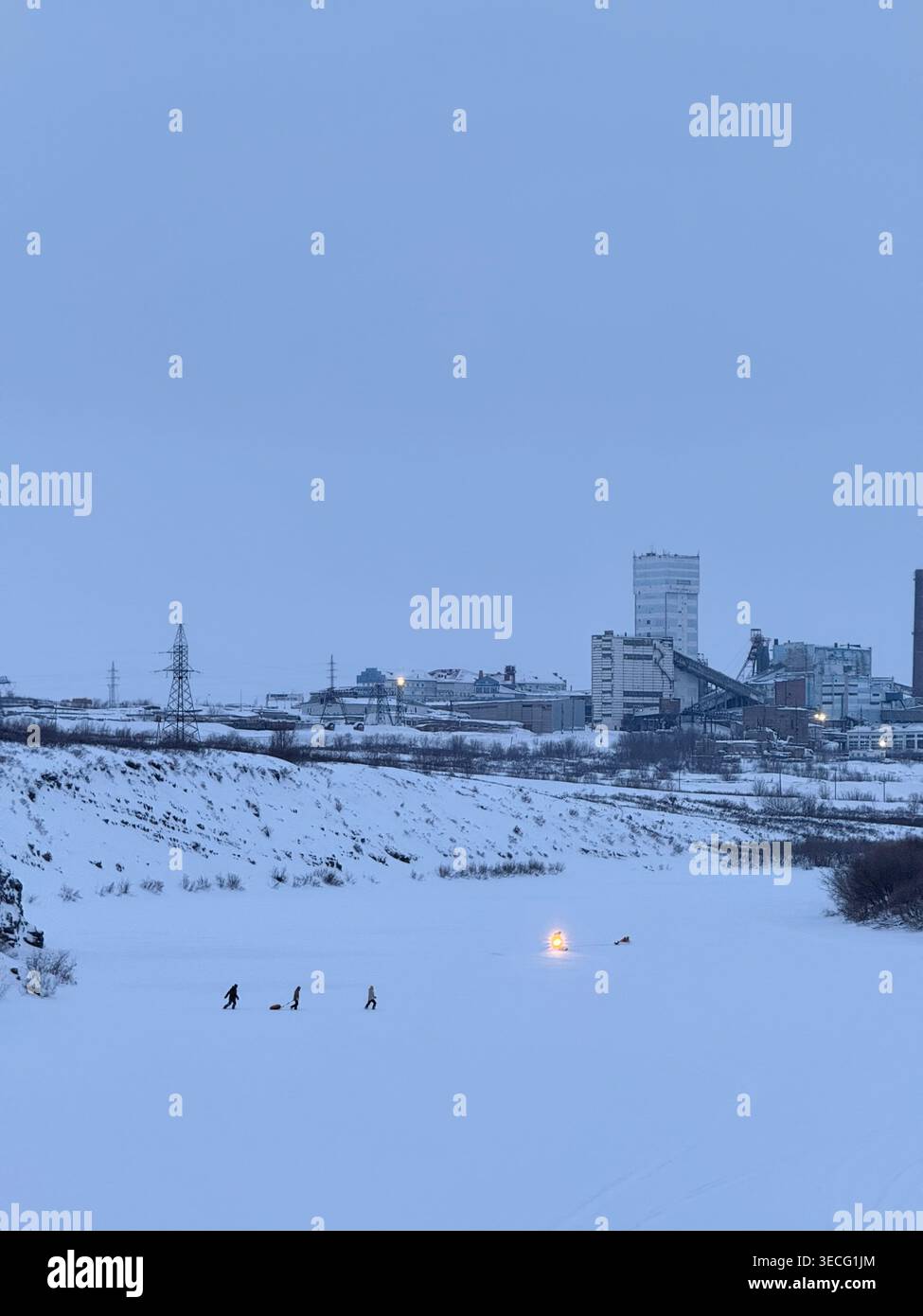Persone che camminano attraverso un fiume ghiacciato vicino a edifici industriali in inverno Foto Stock