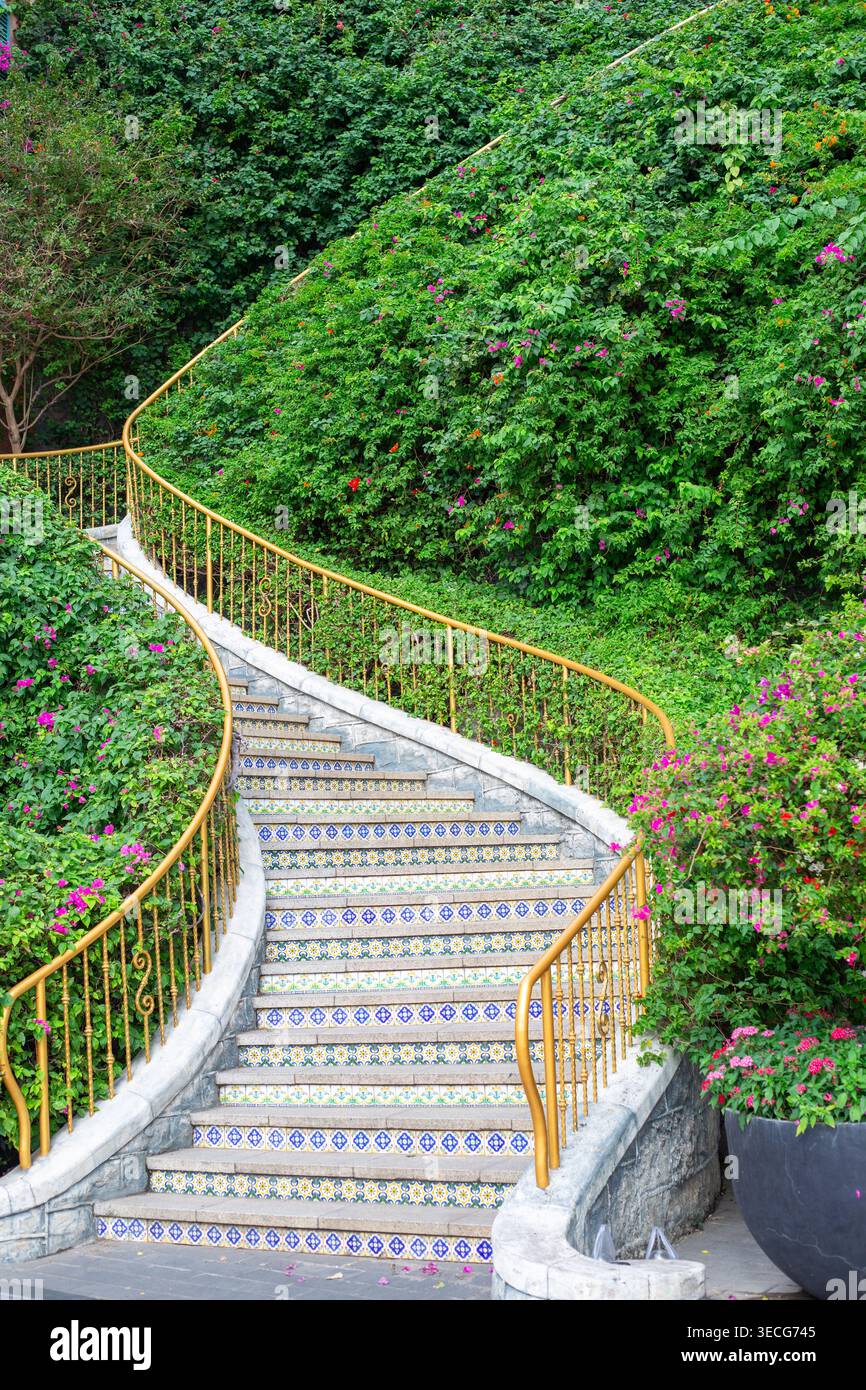 La tortuosa scalinata in pietra con ringhiere gialle conduce su una lussureggiante collina tropicale verde. Giardino tropicale, parco paesaggistico, percorso all'aperto. Foto Stock