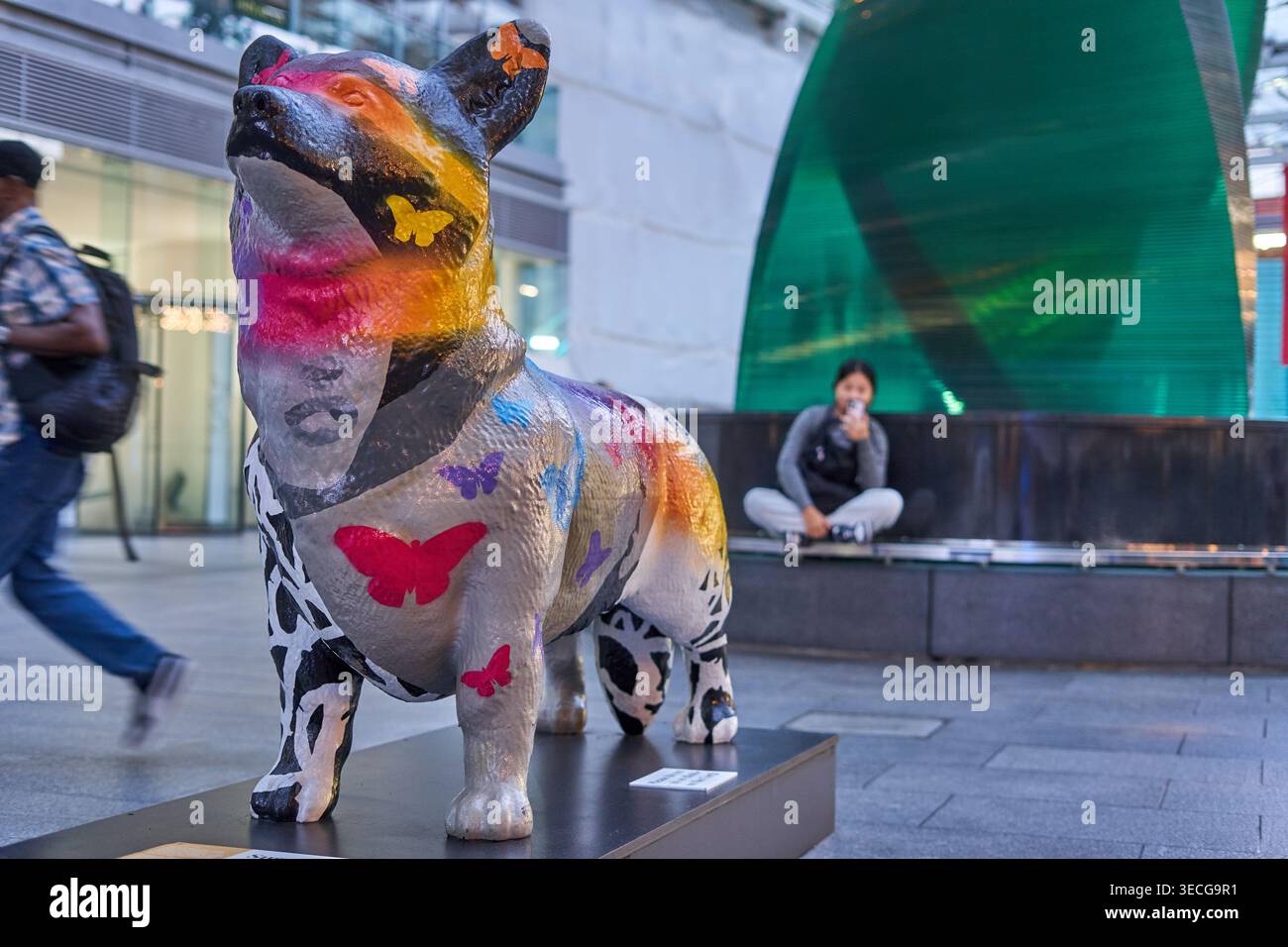 Una statua di cane corgi dipinta con colori vivaci esposta in una piazza urbana a Londra. La scultura presenta disegni artistici vibranti tra cui farfalle in Foto Stock