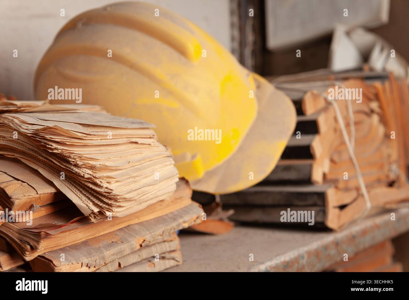Primo piano con profondità di campo ridotta. Il primo piano mostra una pila ben focalizzata di documenti obsoleti e fortemente deteriorati su uno scaffale metallico polveroso. Foto Stock