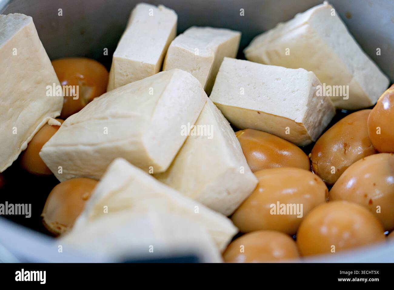 Primo piano di mattoncini di tofu bianchi freschi e uova brasate marinate di soia in una pentola da cucina Foto Stock