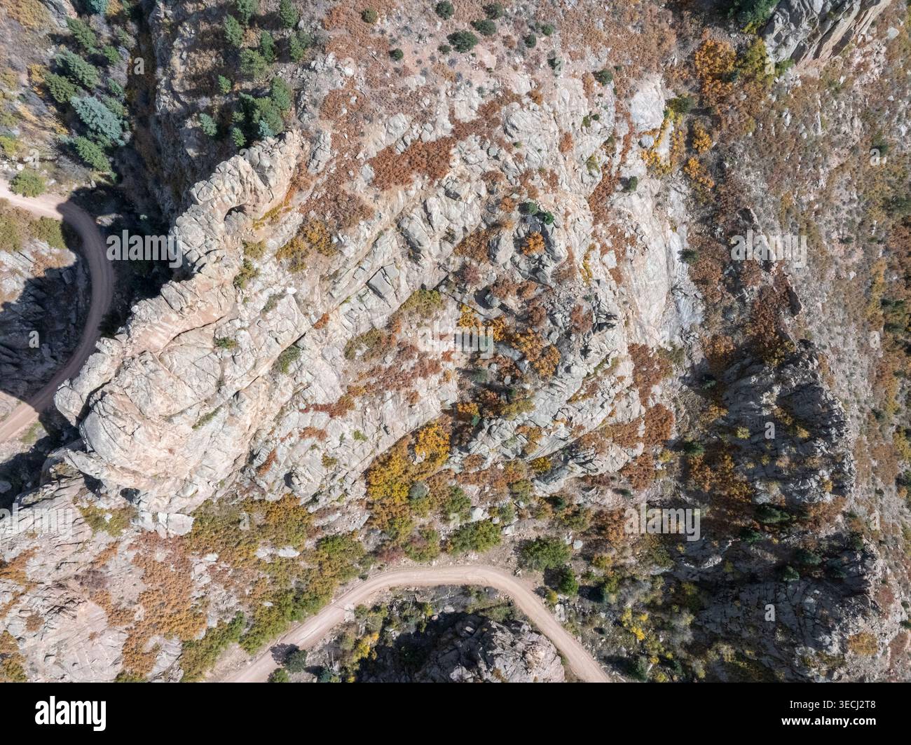 Vista aerea di una ripida scogliera rocciosa con colorate foglie autunnali e una tortuosa strada sterrata attraverso il terreno montano. Foto Stock