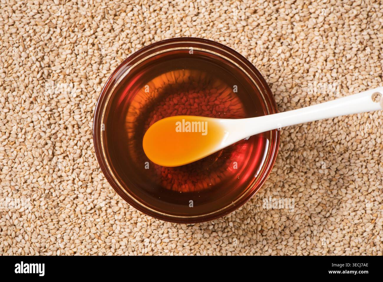Olio di sesamo, un ingrediente salutare, che scorre da un cucchiaio in una ciotola circondata da semi Foto Stock