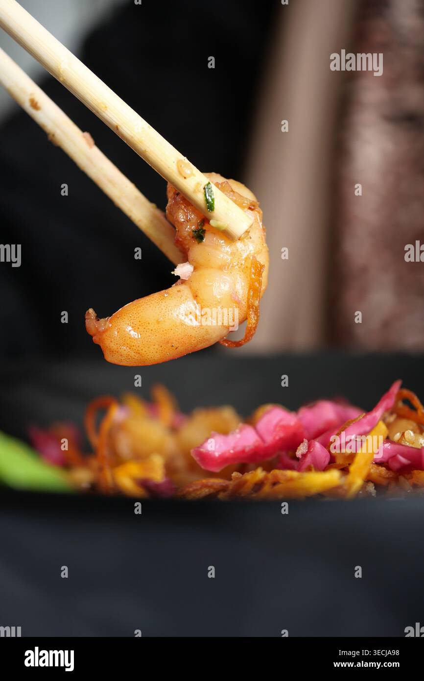 Gamberi tenuti con le bacchette sopra una ciotola di spaghetti Foto Stock